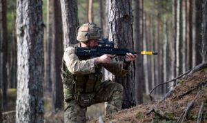 Man dressed in camouflage crouching holding gun