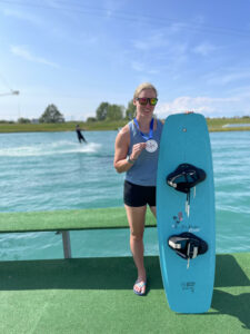 Amy stands with medal and wakeboard in front of water