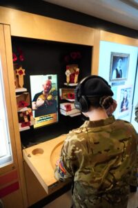 An Army Cadet uses headphones to listen to a veteran's testimony on a Bud interactive screen.