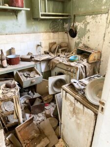 An apartment kitchen in the Central AO of the Nicosia Buffer Zone. The room is filled with abandoned pots, utensils, clothes and furniture, all covered in debris and untouched since 1974.