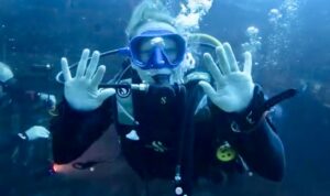 A female Officer Cadet waves to the camera while exploring underwater